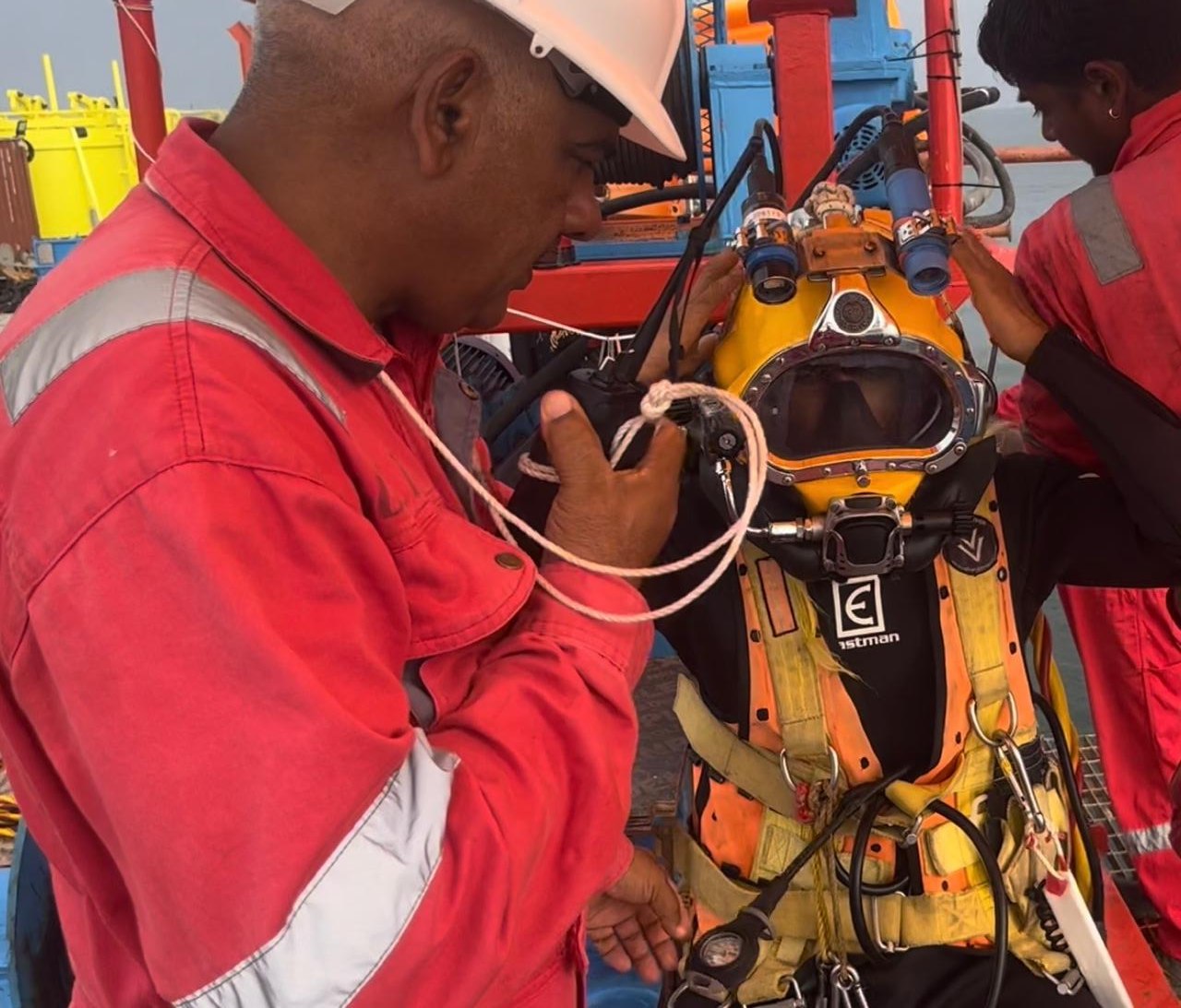 Commercial diver in dive helmet being checked by support crew before a dive