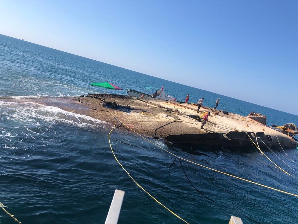 Salvage team working on a grounded, capsized vessel hull at sea