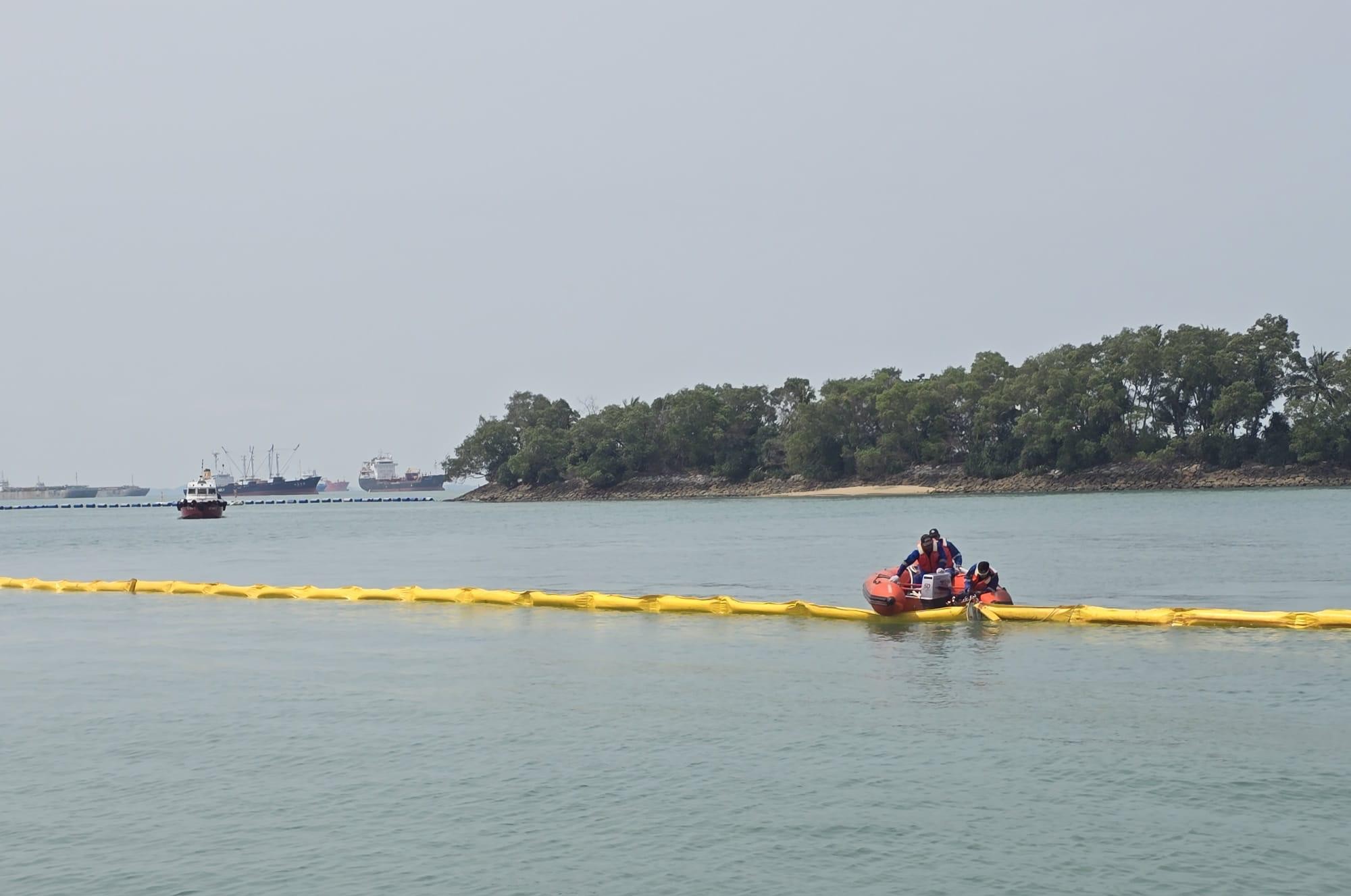 Response crew deploying yellow oil containment booms at sea